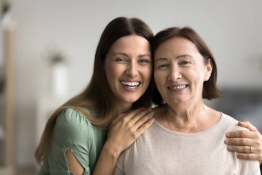 Kameraya poz veren iki farklı güzel kadının kafalarını yakın çekim. Neşeli ve pozitif ifadeli. Anne-kız portresi. Gençlikten bilgeliğe hayat yolculuğu yaşlılık, annelik, aile bağları