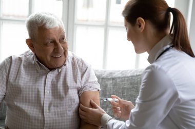 İlgili kadın hemşire, 80 'lerin erkek hastasına koluna iğne yapıyor. İlgili kadın doktor aşısı. Klinikte gülümseyen 70' lerin erkeği, aşı, yaşlı sağlık hizmetleri kavramı.