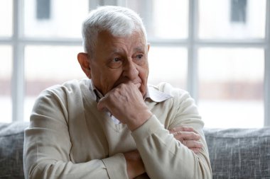 80 'lerin düşünceli büyükbabası oturma odasında kanepede oturur uzaktan düşünür ya da düşünür, düşünceli, üzgün 70' lerin erkeği yalnız hisseder, yas tutar ya da özler, evde iletişim kuramaz.