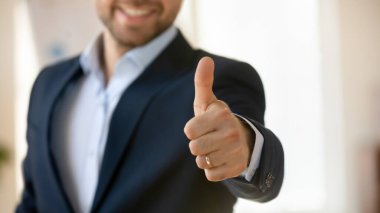 Resmi ceketli genç ve başarılı bir işadamı. Baş parmağını jest gibi gösteriyor. Memnuniyetini ifade ediyor, onaylıyor, olumlu tepkiler veriyor, tavsiye veriyor. Kolunu kapat, afiş atışı.