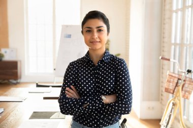 Pozitif güzel Hintli girişimci kadın beyaz tahtası ve büyük masası ile ofiste duruyor, ellerini çapraz tutuyor, kameraya özgüvenle bakıyor. Kendine güvenen iş kadını profesyonel portresi