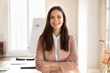 Ofis yönetim kurulunda poz veren başarılı genç işletme koçu elleri bağlı kameraya bakıyor, gülümsüyor. Kadın girişimci, girişimci ve küçük işletme sahibinin ön portresi.