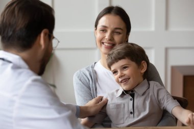 Dost canlısı doktor küçük hasta omzuna dokunuyor, destek ve bakım gösteriyor, sağlık randevusunda karşılıyor, ana kucağında oturan sevimli anaokulu çocuğu, çocuk sağlığı hizmetleri...