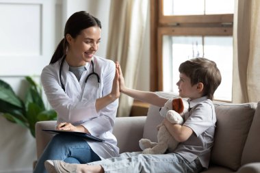 Gülümseyen dost canlısı doktor ve anaokulu hastası beşlik çakıyor, iyi bir sağlık muayenesini kutluyor, küçük çocuğu sağlık muayenesinde karşılayan mutlu bir çocuk doktoru.