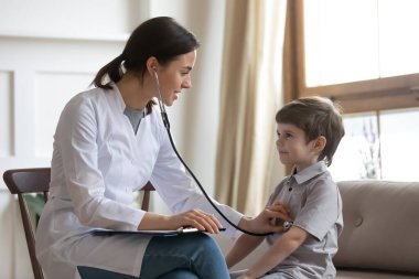 Gülümseyen, dost canlısı bayan çocuk doktoru. Hasta kalp atışlarını ya da akciğerlerini dinleyen anaokulu öğrencisi doktor muayenehanesinde oturuyor, sağlık kontrolü, çocuk sağlığı ve sigorta kavramı.