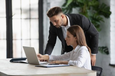 Ciddi erkek takım lideri kadın çalışana bilgisayar işinde yardım ediyor, iş projesi fikrini birlikte tartışıyorlar, çeşitli iş adamları ofiste dizüstü bilgisayarda beyin fırtınası yapıyorlar, takım çalışması kavramı