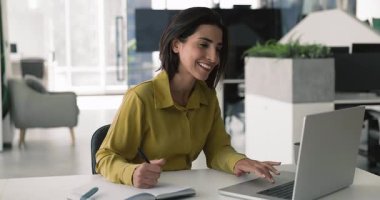 Masada oturmuş dizüstü bilgisayarı kullanan, elinde kalem tutan, kişisel düzenleyiciden notlar alan, ajanda ya da araştırma yapan, randevu ya da teslim tarihleri belirleyen, görev yönetiminde meşgul olan, oluşturan, yazan, yapılacaklar listesi yazan güzel bir kadın.