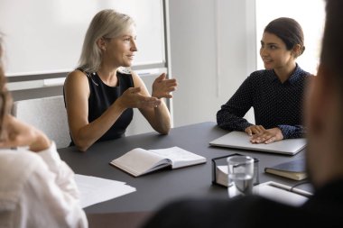 Orta yaşlı iş kadınlarının liderliğindeki modern yönetim kurulunda profesyonel iş toplantısı masa başında personel üyeleriyle oturup şirket hedeflerini veya stratejilerini açıklayacak, genç çalışanlara öğretecek, bilgi ve becerilerini paylaşacak.