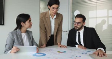 Basılı tablolar ve grafiklerle kaplı konferans masasında işbirliği yapan meslektaşlar, belge verilerinin incelenmesi, bilgilerin analiz edilmesi, çözümlerin stratejisi veya ticari gelişmeler için içgörü geliştirilmesi