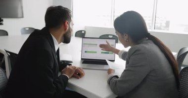 İki profesyonel bilgisayar ekranında gösterilen verileri, performans ölçümlerini, mali verileri, analitik gösterge panellerini, çizelgelerde gösterilen belirli noktaları açıklayan veya vurgulayan çalışma arkadaşlarını tartışıyor