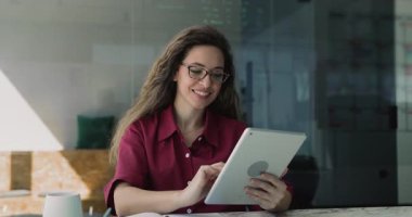 İş yerinde dijital tablet üzerinde çalışan genç iş kadınının portresi, kameraya neşeli bir ifadeyle bakıyor, profesyonelliği yayıyor, ofisteki iş akışındaki modern yapay zeka teknolojilerinden tatmin oluyor