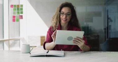 İş kadını yanında fincan ve kişisel organizatör ile birlikte dijital tablet üzerinde sohbet masasında oturuyor, iş e-postalarına yanıt veriyor, sosyal medya platformunu pazarlama amaçlı kontrol ediyor, proje planları veya görevlerini gözden geçiriyor