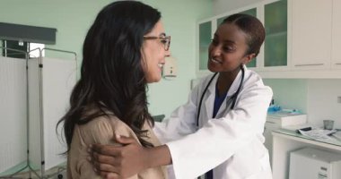 Genç Afrikalı kadın hemşire kliniğe yaptığı ziyarette kadın hasta omuzlarına dokundu, iyi tedavi sonuçlarında iyimserliği teşvik etti, teşvik etti, profesyonel bakım ve destek sağladı