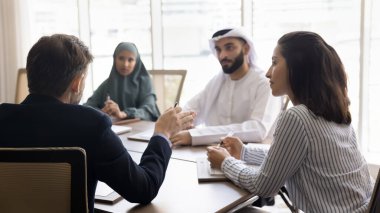 İşadamı masasında çok kültürlü ortaklarla oturuyor, resmi toplantılara öncülük ediyor, hissedarlarla görüşüyor, şirket hedeflerini paylaşıyor, bakış açısını anlatıyor, strateji kuruyor, ofiste işbirliği planlıyor.