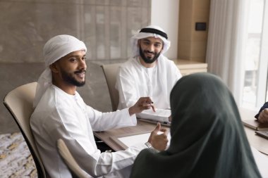 Kandora gibi giyinmiş Arap işadamları ve tesettürlü iş kadını konferans masasının etrafında oturdular, işbirliği, takım çalışması, ortak proje hedeflerinin stratejik sıralaması için toplantı odasında toplandılar.