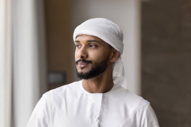 Kendine güveni tam bir Orta Doğulu adam içeride dikiliyor ve düşünceli bir şekilde uzaklığa bakıyor. Genç Arap iş adamı, geleneksel beyaz bulaşık bezi giymiş girişimci, düşünceli bir ifadeyle yan yana bakıyor.