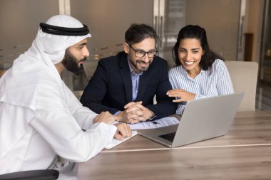 Gülümseyen Avrupalı çift Arap emlakçı veya finans danışmanıyla yaptığı görüşmede dizüstü bilgisayarda sunum izliyor, eşler gözden geçirme teklifi yapıyor, yeni mülk satın almaya, banka ipoteği almaya karar veriyor