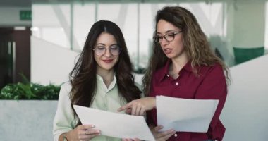 Modern ofiste dokümanları inceleyen, içerik incelemesi yapan, açıklama detaylarını analiz eden, ilerleme ve yazılı bilgilere dayalı sonraki adımları tartışan iki çekici kadın meslektaşım.