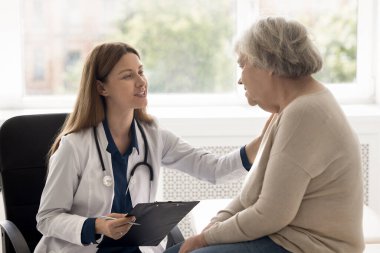 Destek ve empati. Nazik genç bayan doktor, yaşlı bir kadının omuz omuza verdiği terapist klinikte buluşuyor. Rahatlatıcı bir şekilde iyileşme umudu veriyor.