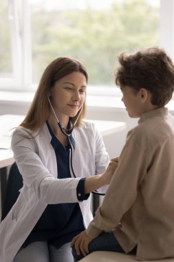 Kardiyoloji kontrolü. Dikey çekim dostu genç bayan doktor steteskoplu çocuk kalbini dinle. Pediatrik kabinede görüştükten sonra bronşit zatürreeden sonra ciğerleri dinle.