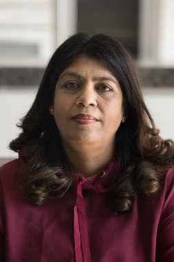 Orta yaşlı ciddi bir Hintli kadının dikey ev portresi. Kameraya gülümseyen bir ifadeyle bakıyor. Kapalı alanda poz veriyor. Olgunluk, bilgelik, eski nesil profil resmi görünümü