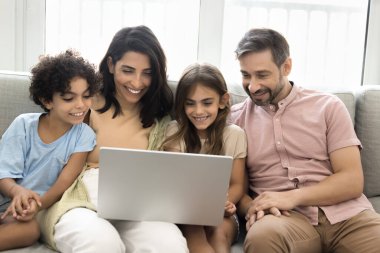 Güzel bir aile kanepede oturup dizüstü bilgisayar kullanıyor, internette eğleniyor, eğlenceli programlar izliyor, eğitim içerikli şeyler ısmarlıyor, bilet alıyor, otel kiralıyor, tatil planları yapıyor.