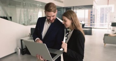 Birlikte dizüstü bilgisayar kullanan, ofis alanına yakın duran, çevrimiçi içeriği izleyen, internet başvuru işini tartışan, yazılım başlatan, gülümseyen, ekrana işaret eden birkaç pozitif iş arkadaşı.