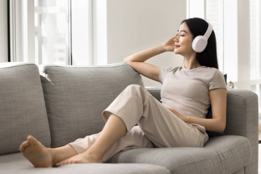 Genç 25 'li yaşlardaki Asyalı rahat kadın favori müzikten hoşlanıyor, modern kablosuz kulaklık takıyor, gözleri kapalı şarkı veya podcast dinliyor, meditasyoncu ve huzurlu görünüyor. Hobi zamanı, hafta sonu evde boş zaman.