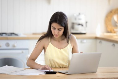 Finansal planlama. Ev idaresinde mali evrak işleriyle uğraşan ciddi genç bir kadın. Hesap makinesi öğrenim belgelerinin faturalarını ödemek için fatura ödemeleri. Kiralık kira ödemelerini not defterindeki bankacılık uygulaması yoluyla yapmak için.