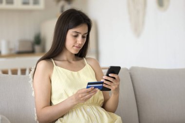 Güvenli internet ödemesi. Odaklanmış gen z kadın mobil bankacılık uygulaması kullanıcısı kanepeye oturur ecommerce pazar yerindeki banka kartından kişisel verileri girerek güvenli çevrimiçi para işlemini telefon kullanarak yapar. Boşluğu kopyala