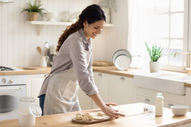 Ev yapımı pişirmek benim hobimdir. Mutfak masasında hamuru saran önlüklü, gülümseyen genç kadın aile kahvaltısı için ev yapımı çörekler hazırlıyor. Pişirilmiş tatlı pişirmenin keyfini çıkarın. Boşluğu kopyala