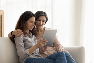 Tüm nesiller için dijital çağ. Yetişkin bir kızla ilgilenmek olgun bir anneyle kanepeye oturmak sosyal medya hesabı oluşturmak için tablet bilgisayarın nasıl kullanılacağını öğretmek.