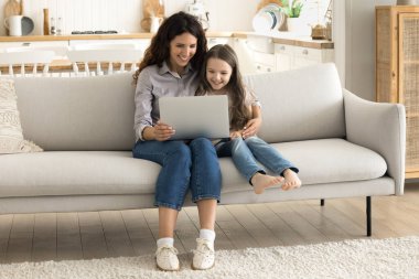 Dijital eğitim. Bin yıllık anne bebek bakıcısı kucuk kiziyla kanepede oturur, ortaokul cocuklariyla birlikte defter bilgisayarinda egitim oyunu oynar, internetten ögrenme uygulamasini kullanarak web 'de bilgi toplar.