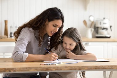 Annemle kolay öğreniyorsun. Bakımlı genç anne dadı mutfak masasında otururken sessiz eğitim faaliyetlerinde olan erken yaşta kız öğrencilere kağıt albümde renkli çizimler yapmayı öğretir.