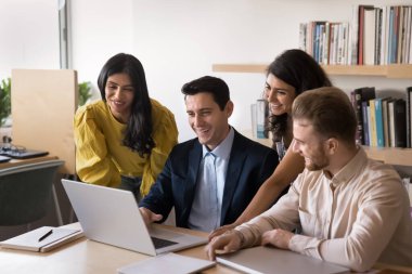 Modern teknoloji akademik çalışmada. Kendine güvenen genç profesör akıl hocası kütüphane masasında bilgisayar başında oturuyor. Çevrimiçi uygulama kullanan çok ırklı küçük bir grup öğrenciyle birlikte proje üzerinde çalışıyorlar.