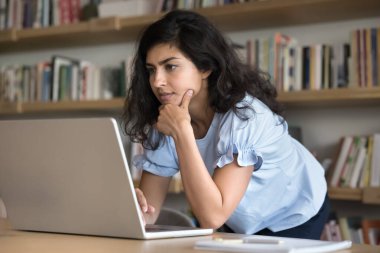 Eğitimde dijital yaş. Ciddi genç lise öğrencisi kütüphanede proje üzerinde çalışıyor. Bilimsel sorunları çözmek için web kaynakları veritabanlarını kullanın. Not defteri üzerinden grup araştırmalarına katılın.