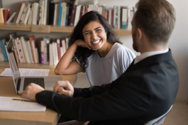 Arkadaşlık ve ortaklık. İki genç öğrenci, çeşitli cinsiyet çeşitliliğine sahip gruplar halinde bilimsel proje üzerinde çalışırken eğleniyorlar kütüphanede not defteri kullanarak araştırmayı tartışırken gülüyorlar.