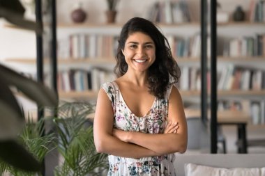 Rahatlık ve güven. Mutlu bir portre, sıradan giyinmiş güzel bir genç kız serbest çalışan küçük işletme sahibi sıcak ofis kitapçısında kollarını kavuşturmuş kameraya bak.