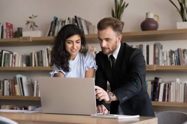 Akıl hocasının destekleyici rolü. İlgili bayan öğrenci, genç erkek öğretmen asistanının deneyimli meslektaşlarıyla işbirliği içinde kütüphanede e-öğrenim uygulamasında iş detaylarını göstermesini dinliyor.