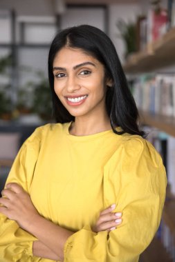 Başarı ve güven. Dikey portre güzel gülümseyen motivasyonlu genç bayan öğrenci ofis yerinde kollarını kavuşturup kameraya bakarak günlük giysiler giyer ve başarılarından gurur duyar.