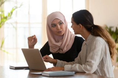 Melez ırk ve ortadoğu kökenli kadın meslektaşlar veya öğrenciler modern ofis veya sınıfta birlikte çalışarak öğrenim görüyorlar. Takım çalışması, işbirliği, ortak proje kavramının gerçekleştirilmesi
