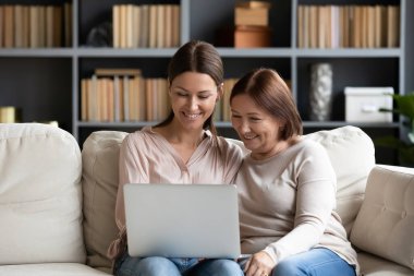 Yetişkin bir kız çocuğu, yaşlı bir anneye bilgisayar kullanımı konusunda yardım ediyor, video araması yapıyor, kanepeye oturup internetten alışveriş yapan çok nesilli kadın ailesini gösteriyor, internet kavramında kolay hizmetlerden faydalanıyor.