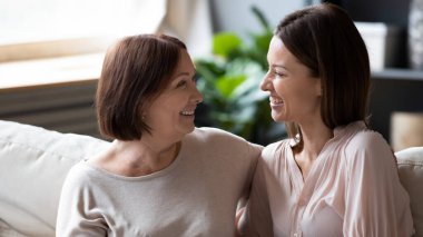 Yatay bakış açısı orta yaşlı anne 30 'lu yaşlardaki yetişkin kız kızlarına bakıyor oturma odasında kanepede oturan kadınlar kalp kalbe konuşmalar yapıyorlar, iyi sıcak ilişkileri destekliyorlar farklı nesiller kadın kavramını destekliyorlar.