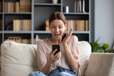 Neşeli kadın kanepede oturup akıllı telefondan mesaj okurken şaşırır. Etkinlik davetiyesi almak, alışveriş yapan kişi indirimlerden, satış fırsatlarından, e-ticaret kullanıcılarından hoşlanır. Çevrimiçi piyango kazanan konsepte bahis oynarlar.