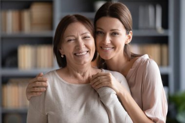 Farklı kuşaklardan akrabalar oturma odasında kameraya bakan kadınlar, yetişkin kız çocuğu yaşlı anneye sarılıyor, sevgi kavramı, koruma, yetişkin çocuk ve ebeveyn arasındaki sıcak ilişkiler.