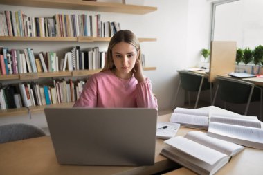 Masada dizüstü bilgisayar kullanarak oturan, kütüphanede tek başına okuyan, araştırma yapan, birden fazla eğitici internet kaynağı kullanarak yararlı bilgiler arayan kız öğrenci. Giriş, sınav hazırlığı.