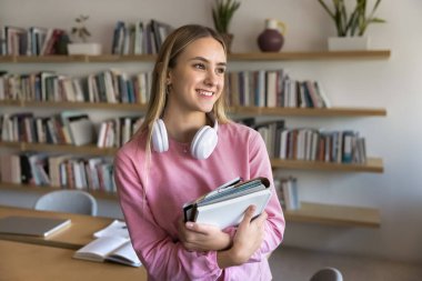 Çekici Avrupalı öğrenci ders kitabını elinde tek başına üniversite ya da okul sınıfında duruyor, mutlu bir gülümseme ve rüya gibi bir ifadeyle bakıyor, hayal kuruyor, üniversiteye kabul edilmeyi düşünüyor.