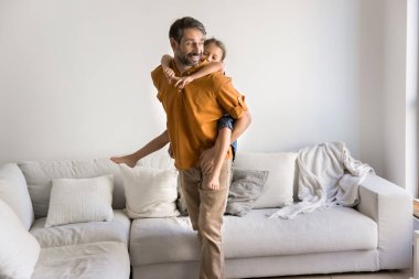 Sevgi dolu orta yaşlı bir baba, sevimli 6 'lı yaşlarındaki kızını sırtında taşırken modern oturma odasında durmuş, evde birlikte sırtında oynuyorlardı. Evde oyun zamanı rutini, mutlu babalık.