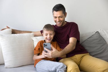 Baba ve küçük oğlu internetteki boş zamanlarını modern akıllı telefonları kullanarak geçiriyorlar, eğlendirici içerikler izliyorlar, oyun oynuyorlar ya da yeni uygulamalar öğreniyorlar. Evde boş vakitlerde modern teknoloji kullanımı
