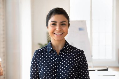 Genç, kendine güvenen Hintli iş kadını rahat bir bluz giyiyor ofiste tek başına duruyor, profesyonellik ve başarı yayıyor, memnuniyet duyuyor, yaptığı işten memnun görünüyor, vesikalık fotoğrafı.